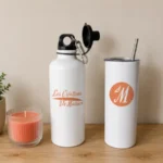 Gourde et mug personnalisés avec le logo Les Créations de Maïwen présentés dans un décor minimaliste avec une bougie et une plante.