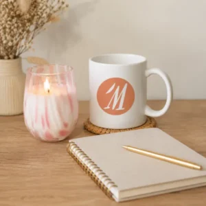 Décor minimaliste avec une bougie artisanale marbrée, un carnet de notes et un mug personnalisé au logo Les Créations de Maïwen sur une table en bois.